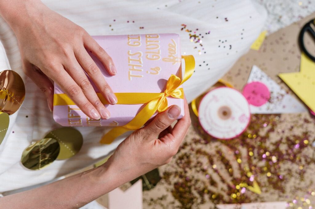 A festive gift wrapped with a yellow ribbon and the message 'This gift is gluten-free' amidst sparkles and decorations.